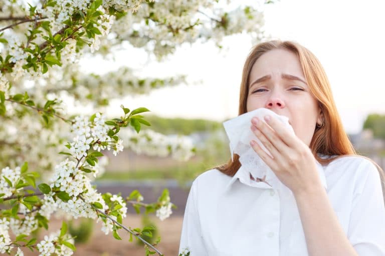 woman in the middle of sneeze with a tissue to her face, outdoors