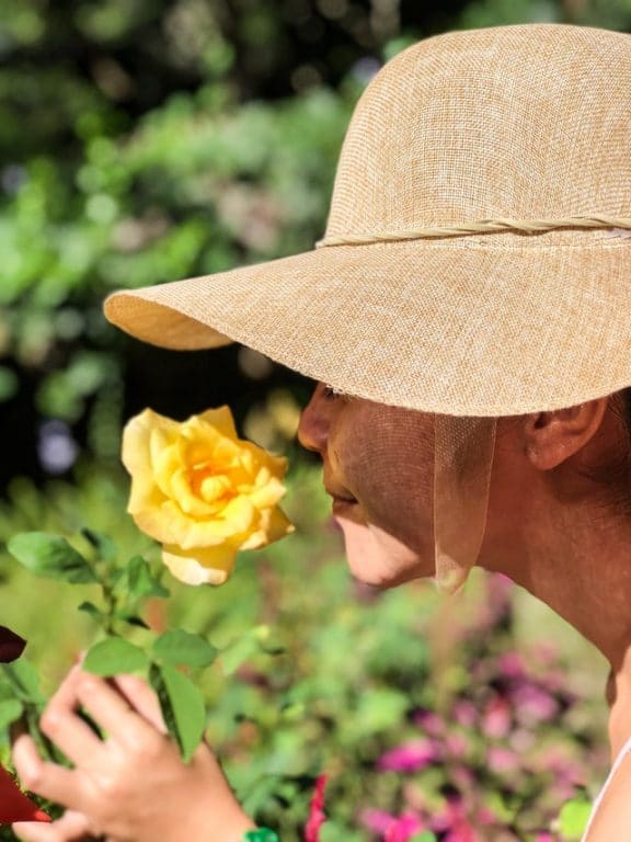 woman-wearing-sun-hat-smelling-yellow-rose
