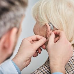 Audiologist fitting hearing aid to woman's ear.