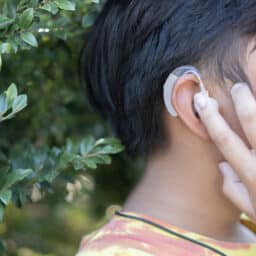 Boy touches hearing aid in park