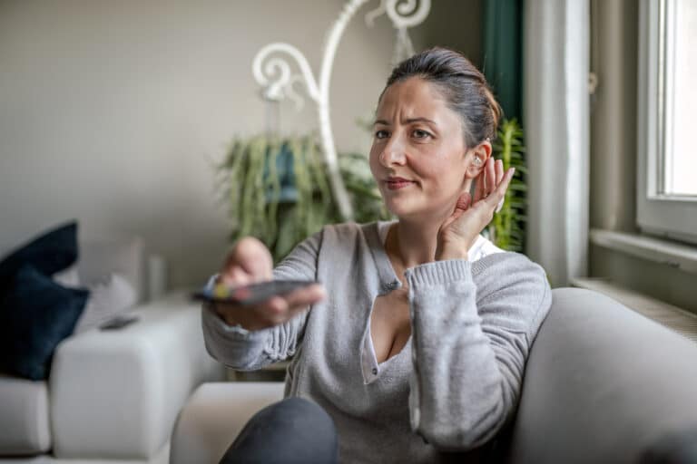 Woman cups ear behind hearing aid