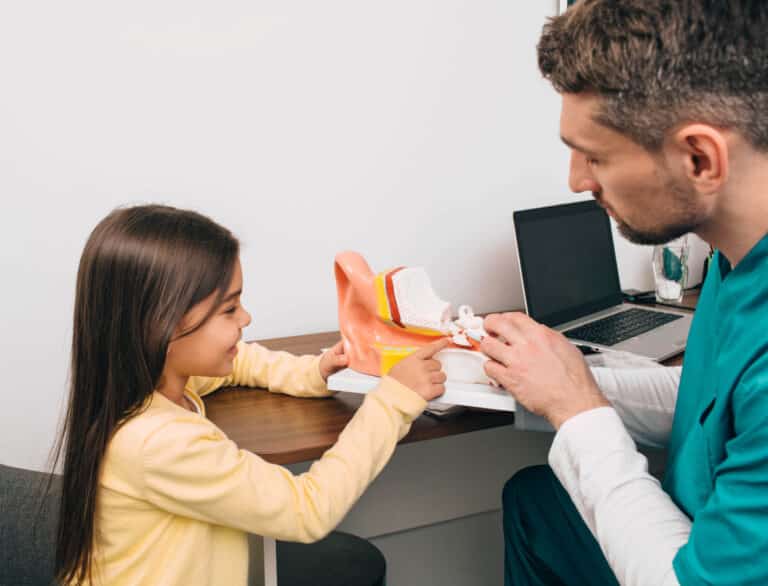 Young girl looking at a model of an ear with her audiologist.